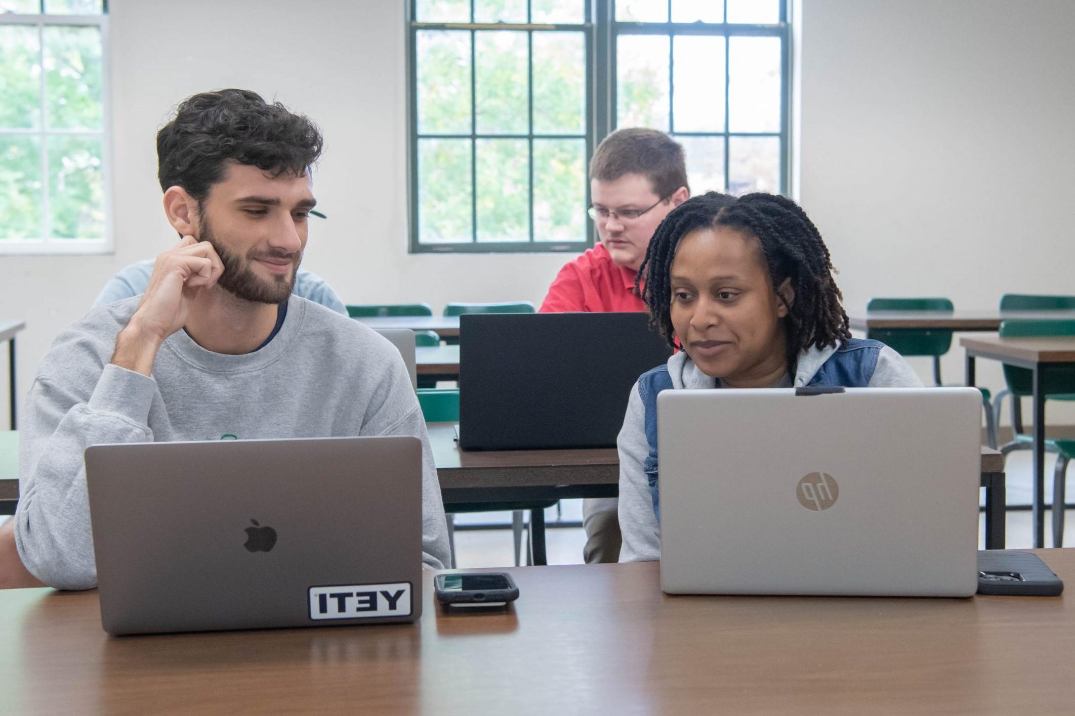 Three students looking at each others laptops in a classroom.